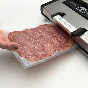 Salami packed in a vacuum sealer bag entering a vacuum sealer